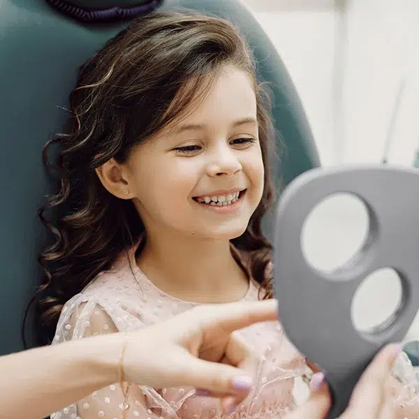 Young girl smiling at her reflection at first orthodontic appointment